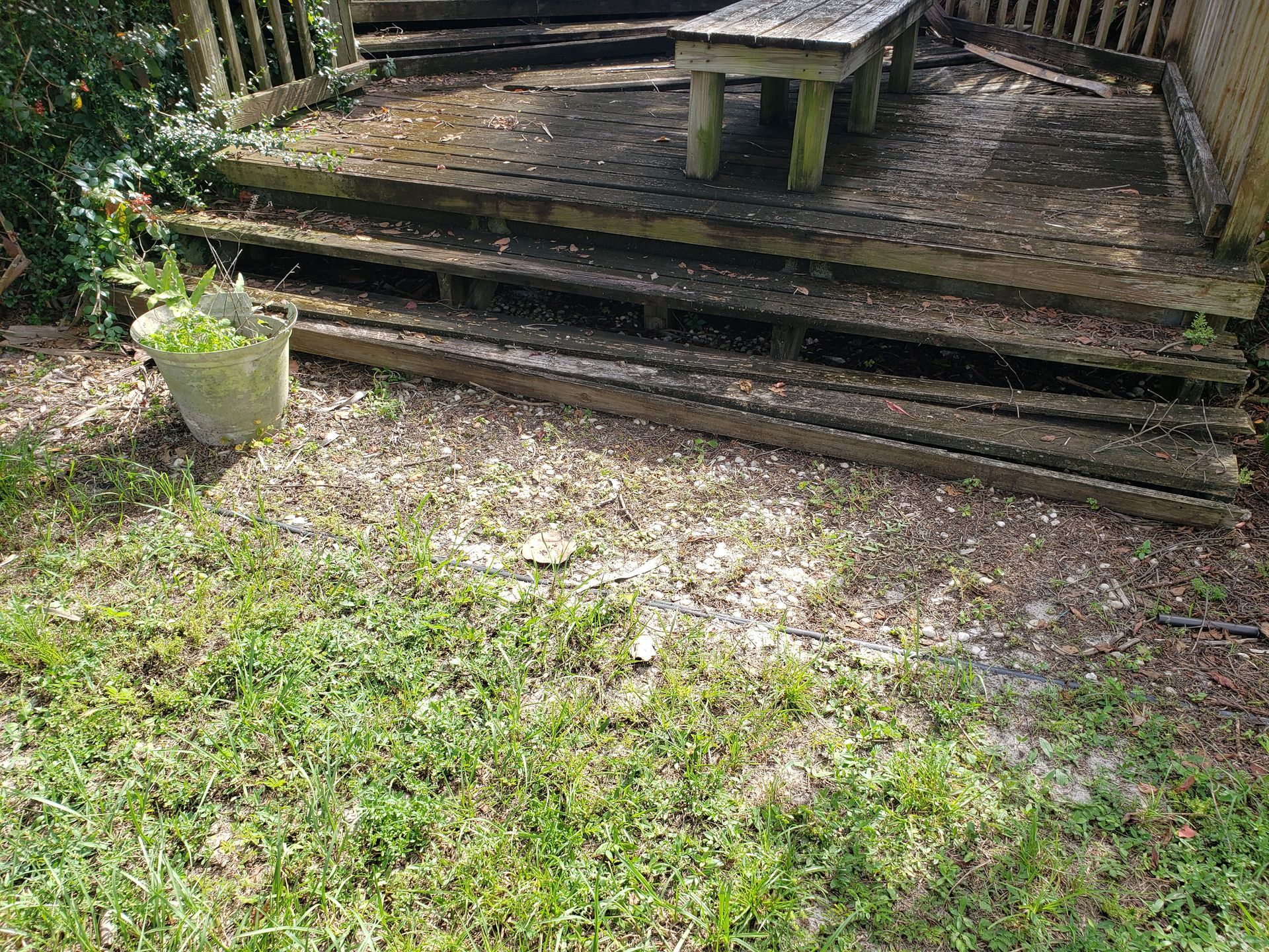 Weathered wooden deck with steps, a small table, and a potted plant beside a grassy yard.
