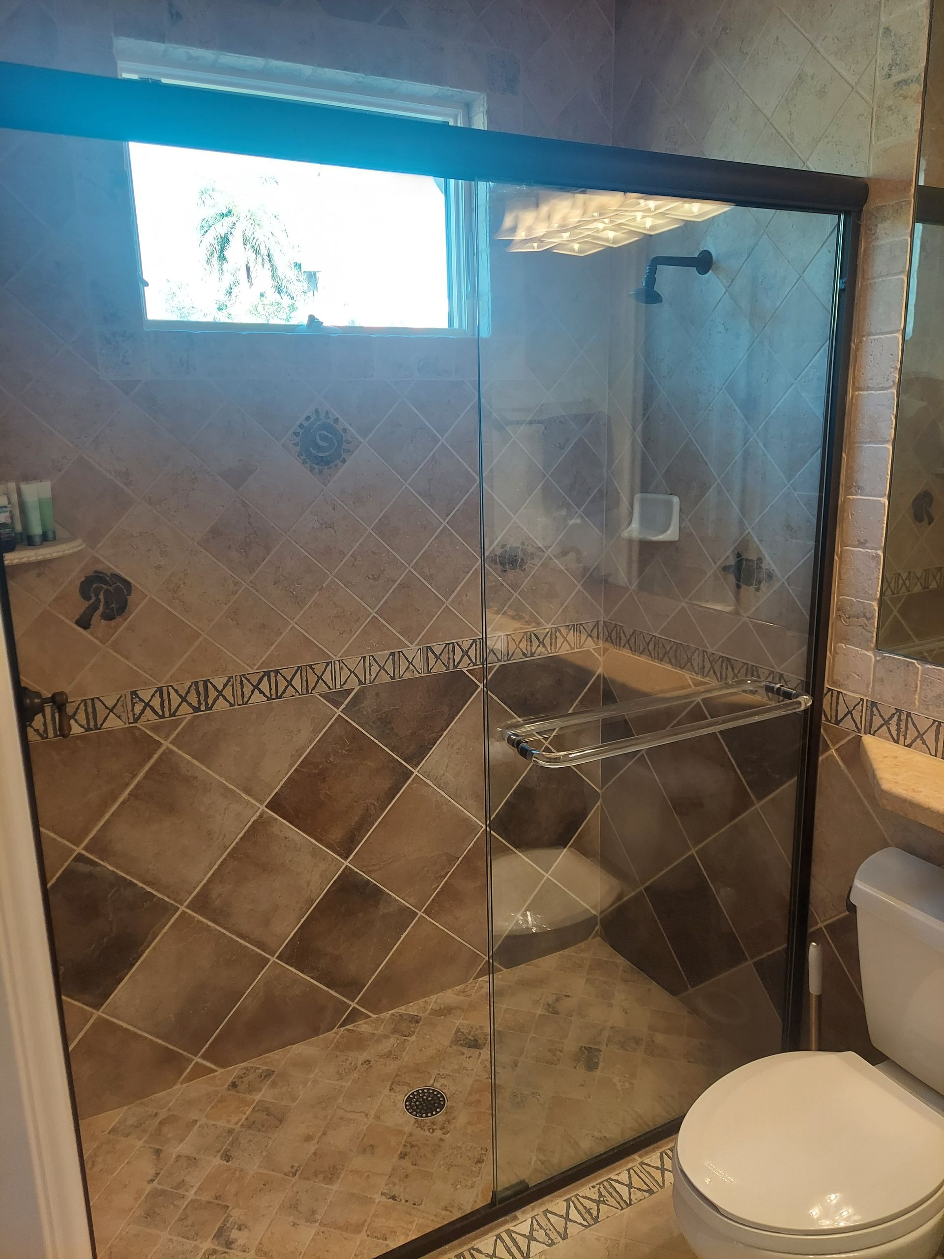 Bathroom with a glass shower enclosure, tan tile walls, and a toilet in the foreground.