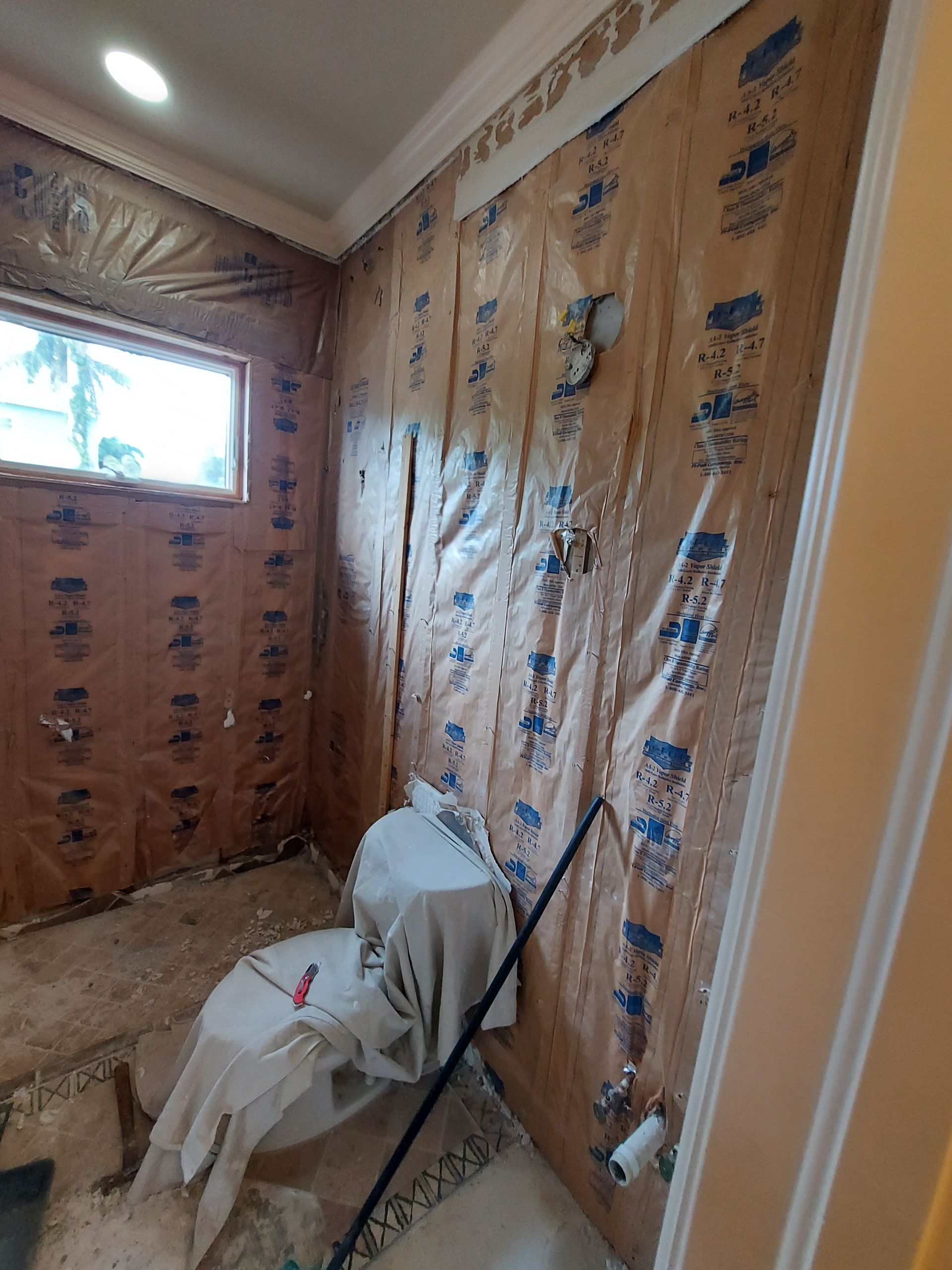 Partially finished bathroom with pink wall panels, window, and a toilet covered in plastic sheeting