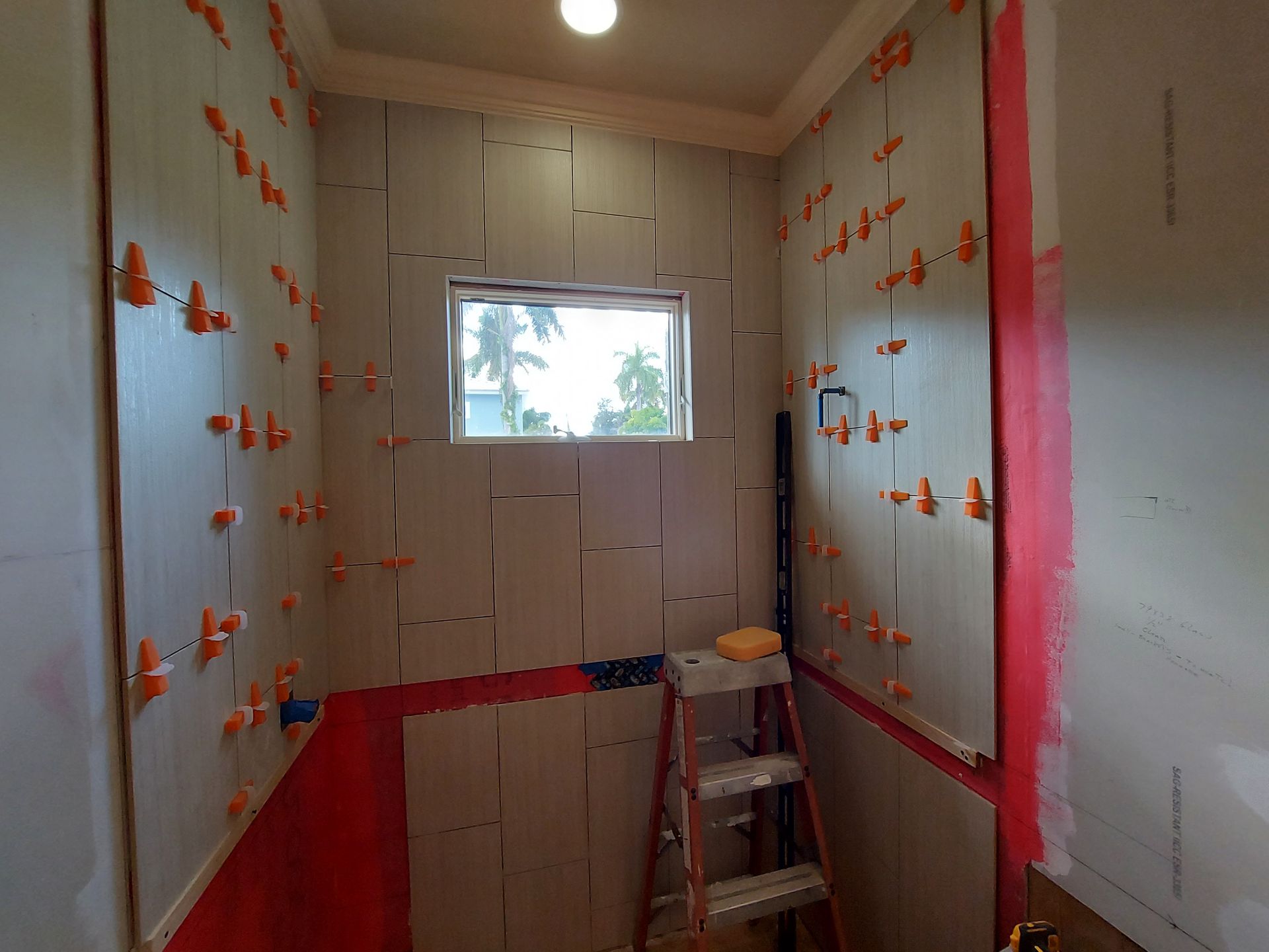 Unfinished small bathroom under renovation with white insulation panels, red tape, and a ladder below a window.