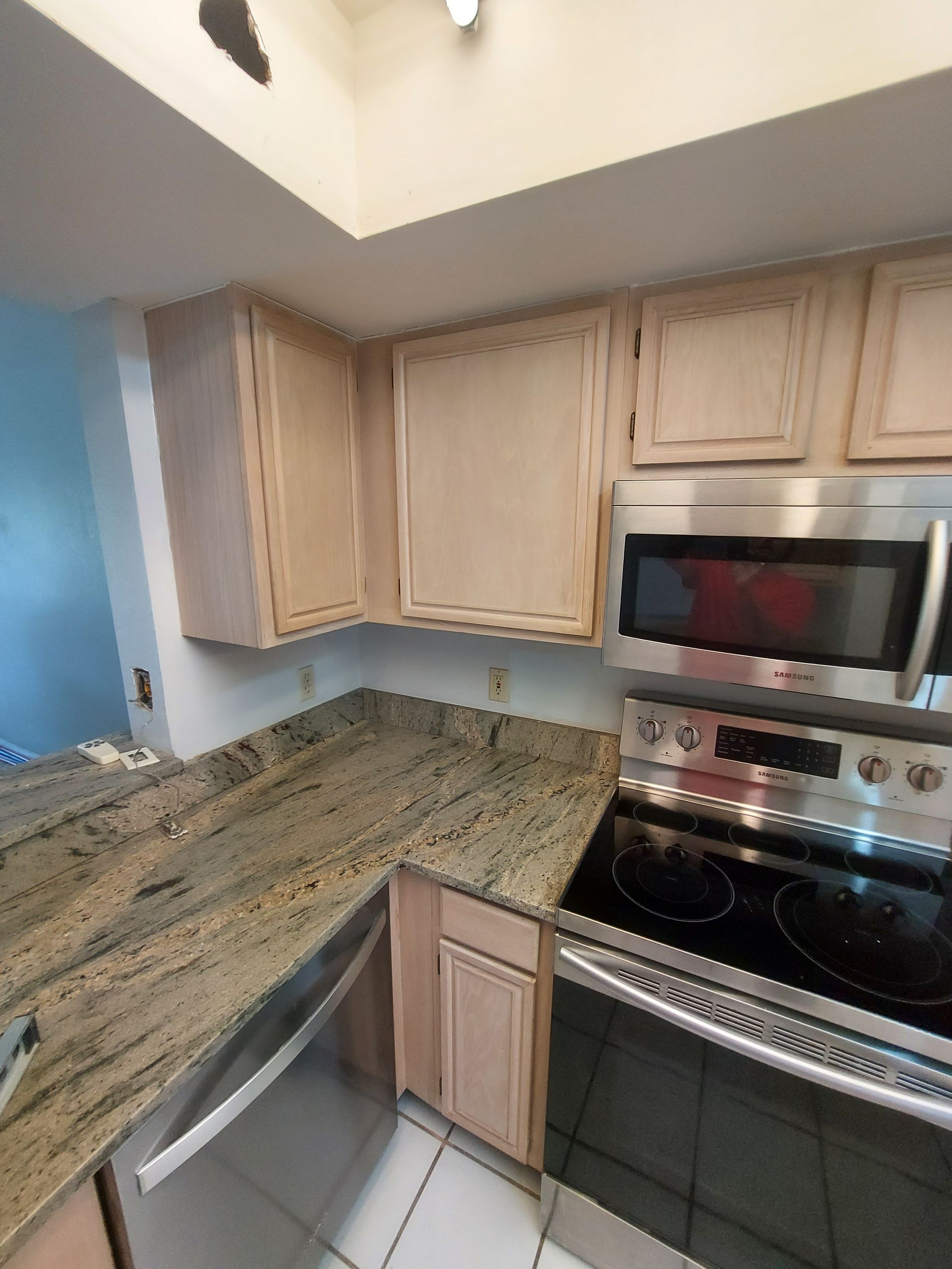 Compact kitchen with light wood cabinets, granite counters, and stainless steel stove and microwave.