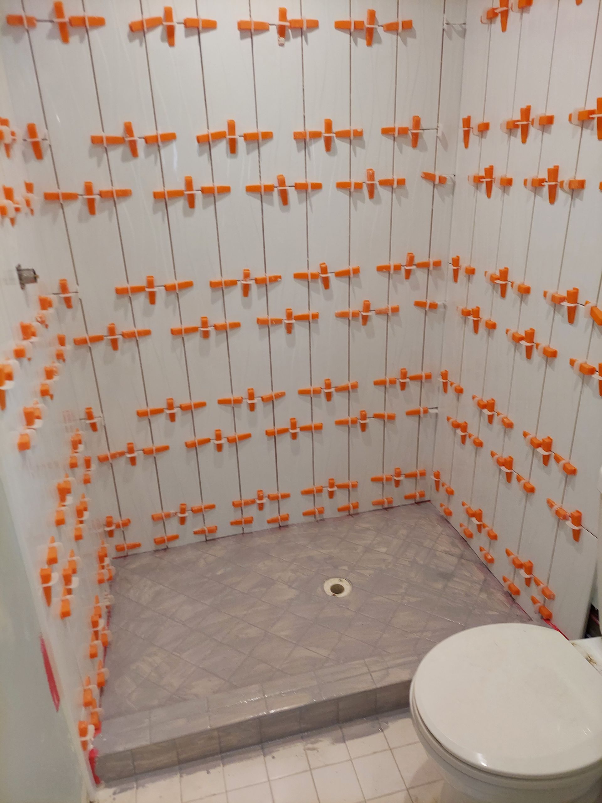 Tiled shower under construction with orange spacers and a white toilet in the foreground