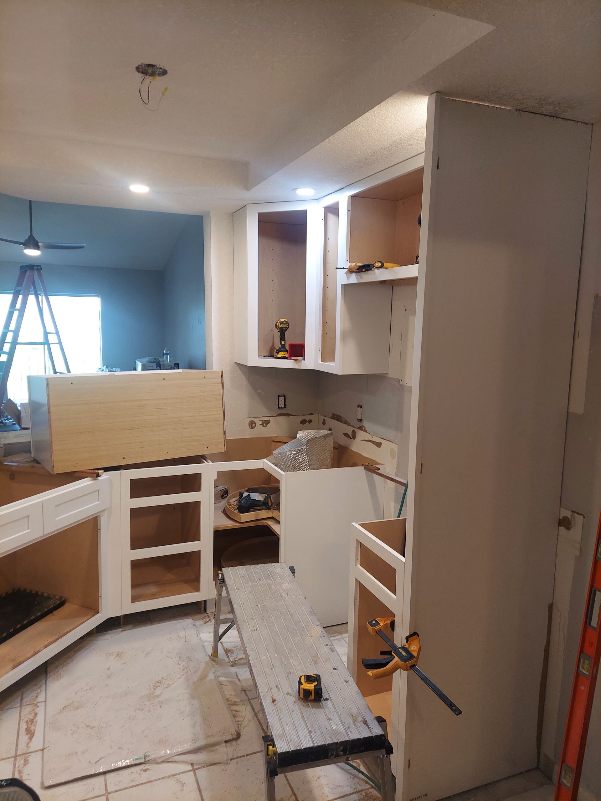 Partially renovated kitchen with unfinished white cabinets, countertop tools, and a ladder in the background