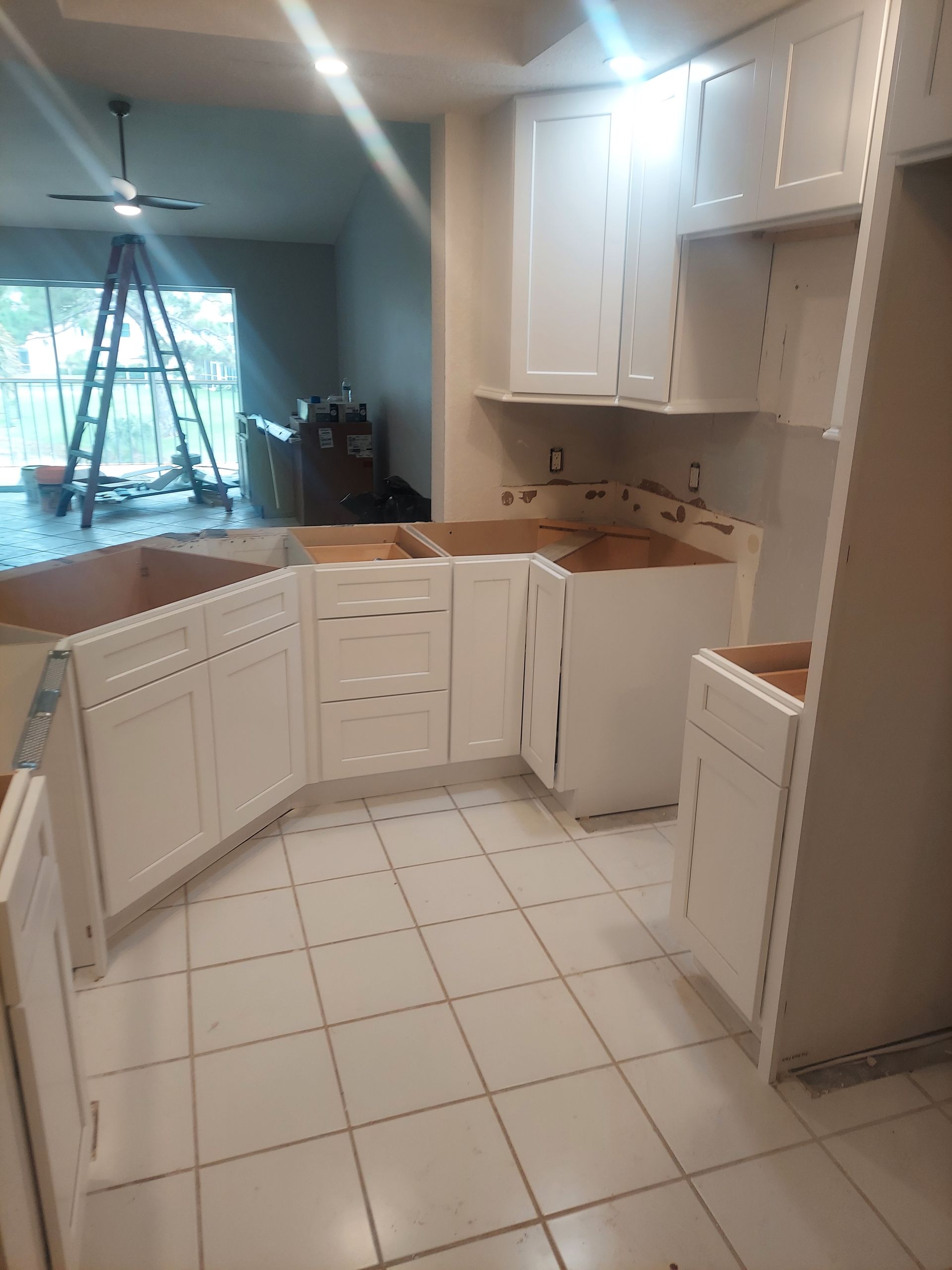 Small white kitchen with tiled floor, cabinets, and a view into a bright living room.