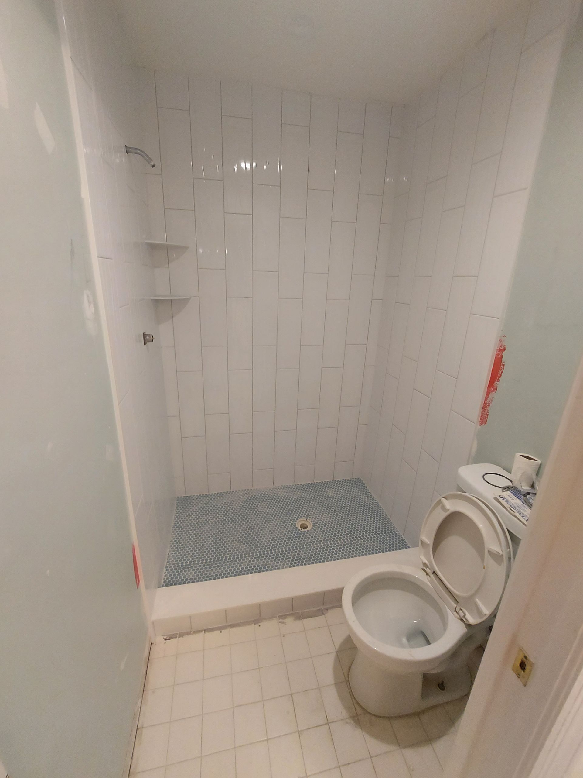 Small tiled bathroom with a toilet and shower stall, blue bath mat on the floor.