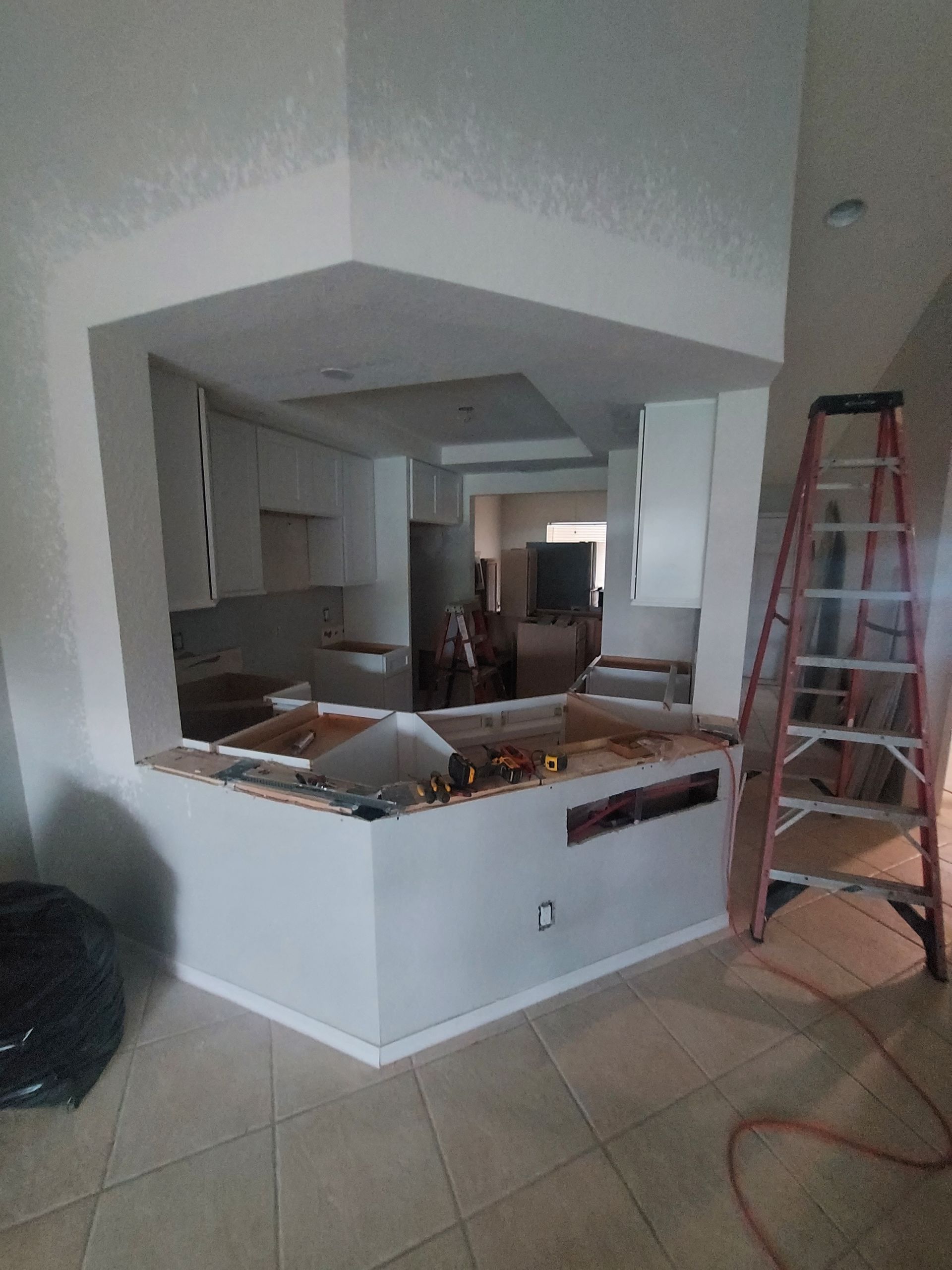 Partially demolished kitchen pass-through with exposed cabinets, debris, and a red ladder in a tiled room