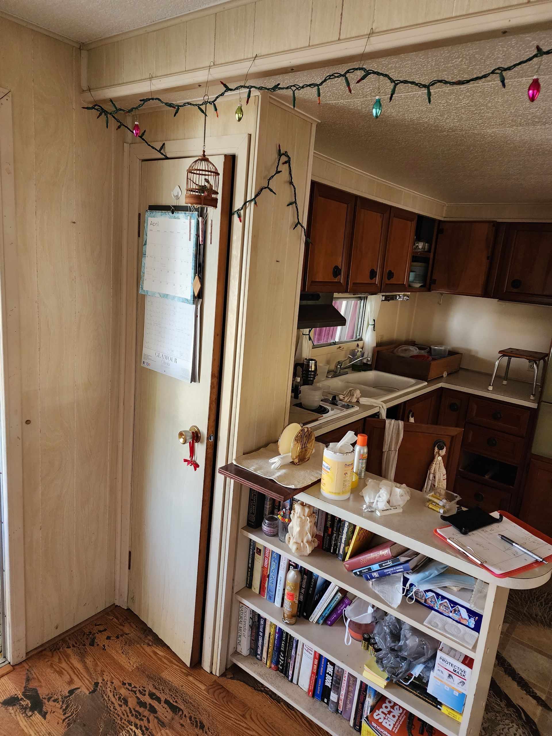 Small kitchen with wooden cabinets, a white fridge, and a shelf of books and dishes in the foreground