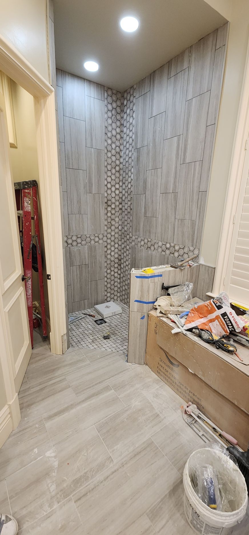 Narrow hallway under renovation with patterned wallpaper, recessed lights, and tools and materials stacked on the right