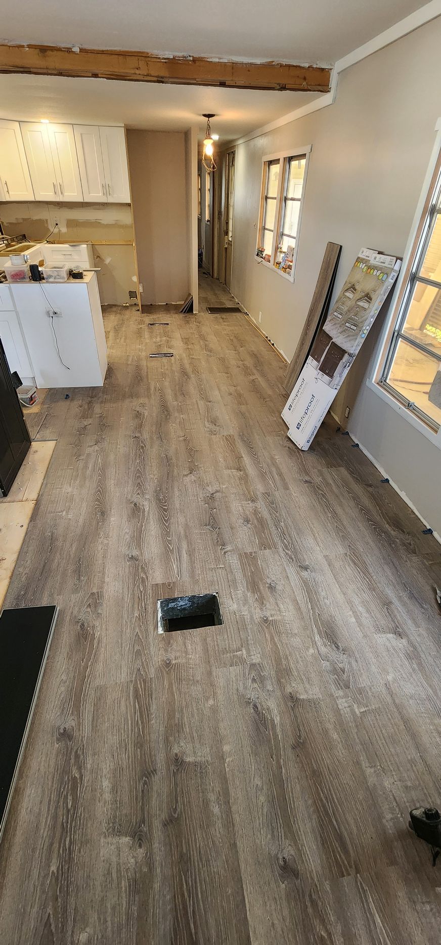 Empty room with wood-look flooring, white walls, and a window on the right during renovation.