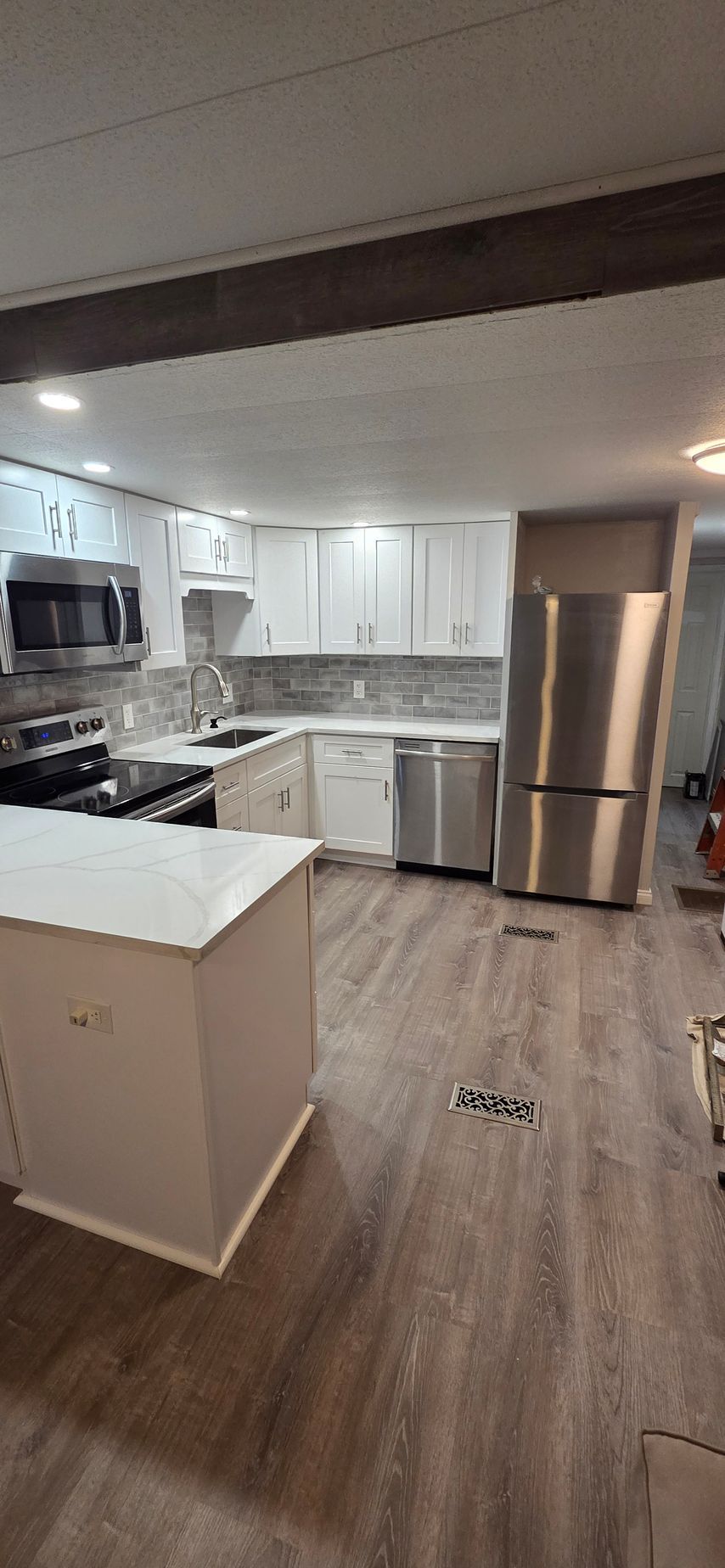 Modern kitchen with white cabinets, stainless steel refrigerator, gray countertops, and wood-look flooring.