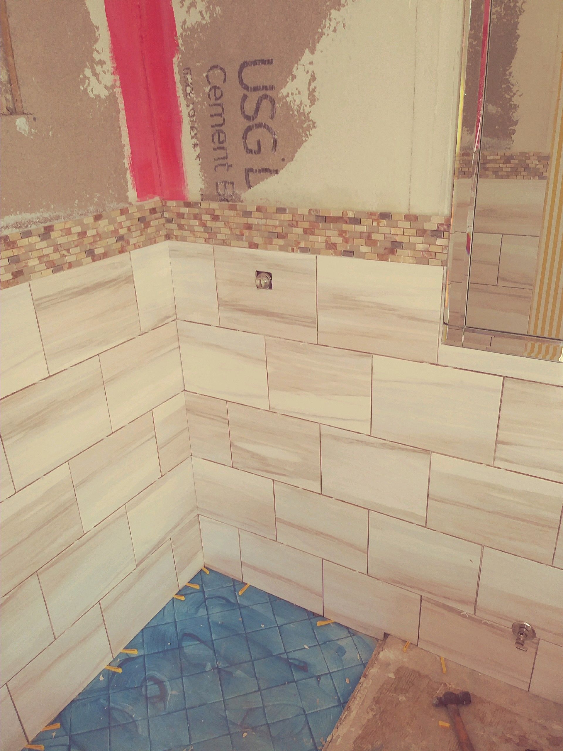 Tiled corner of a room with white subway tiles, blue floor, and a partially finished wall above.