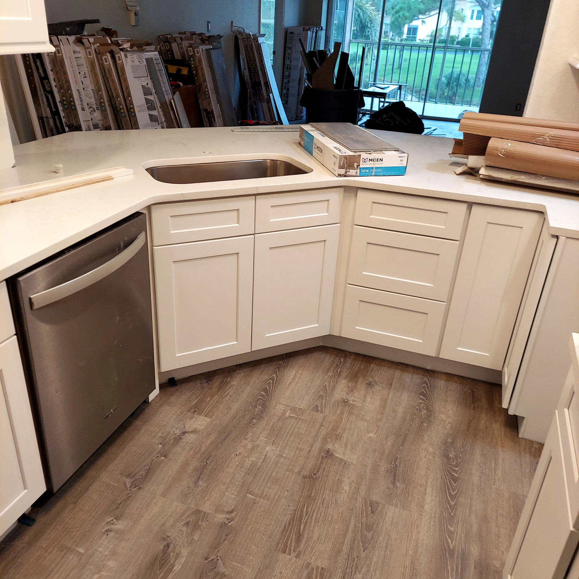 White kitchen with curved island cabinets, wood-look floor, and stainless dishwasher under construction