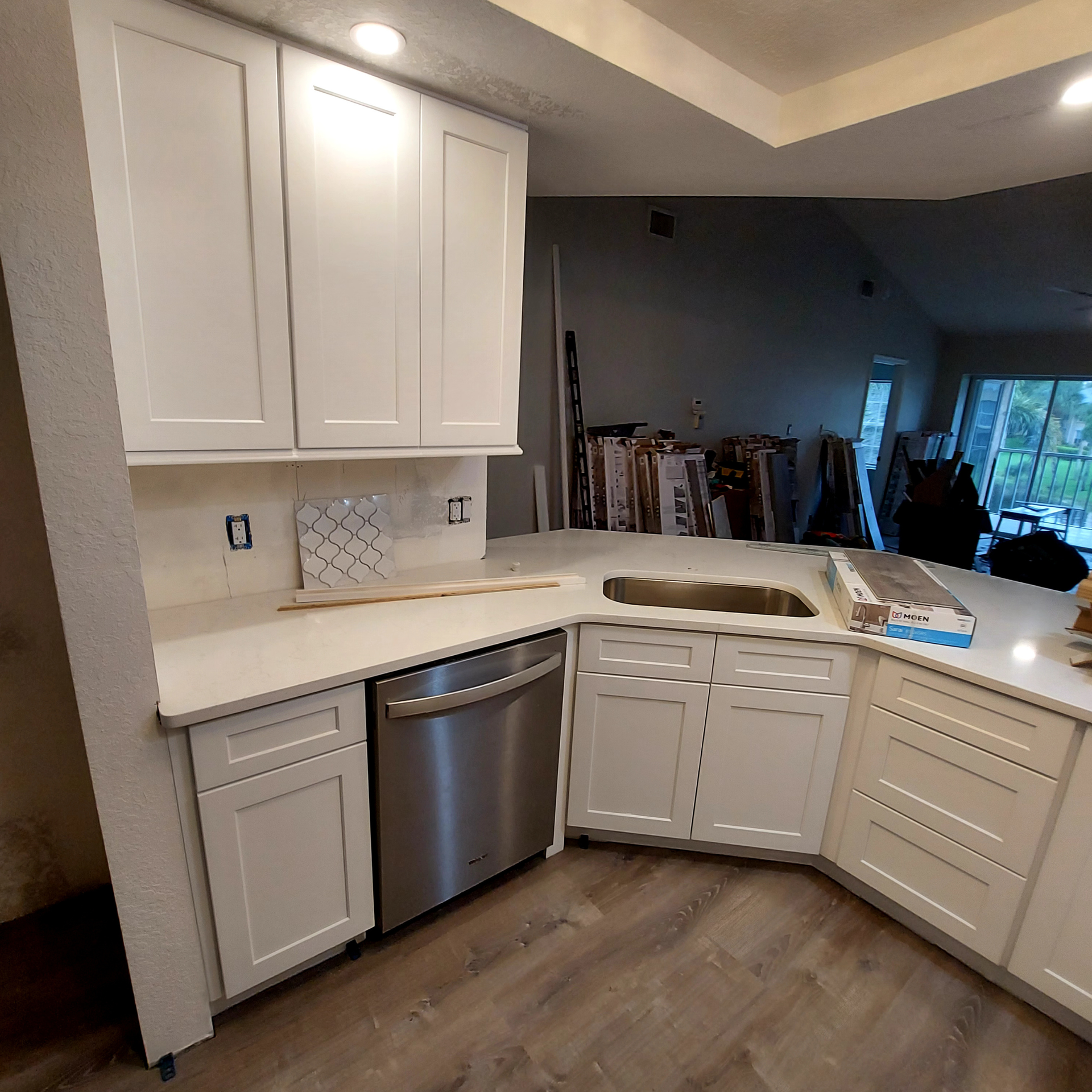 Modern kitchen with white cabinets, stainless dishwasher, corner sink, and wood-look flooring.