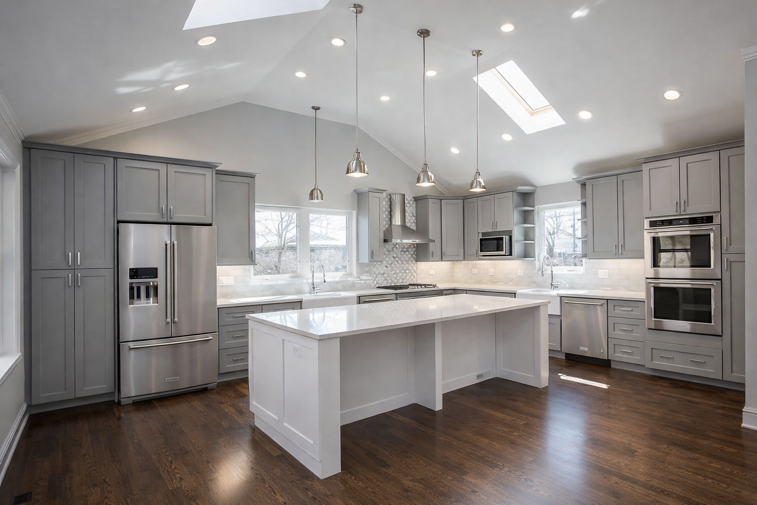 Modern kitchen with gray cabinets, a white island, stainless steel appliances, and skylights under a vaulted ceiling.