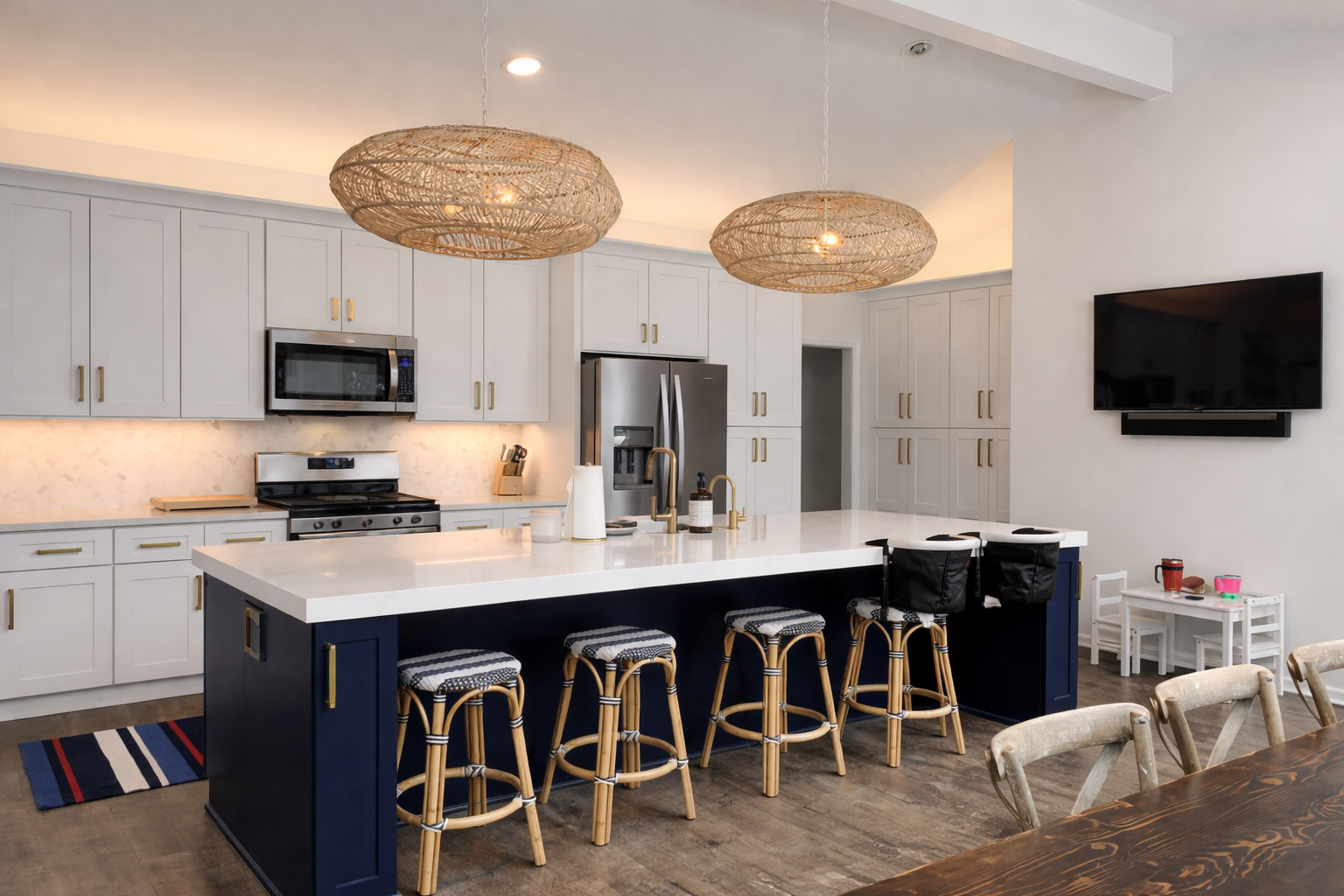 A modern kitchen with white cabinets, a large navy blue island with four stools, and two round woven pendant lights.