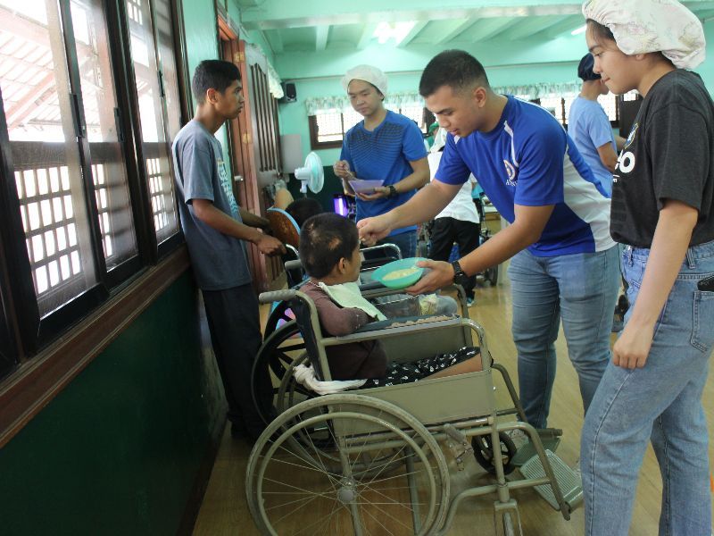 A man in a blue shirt is feeding a woman in a wheelchair