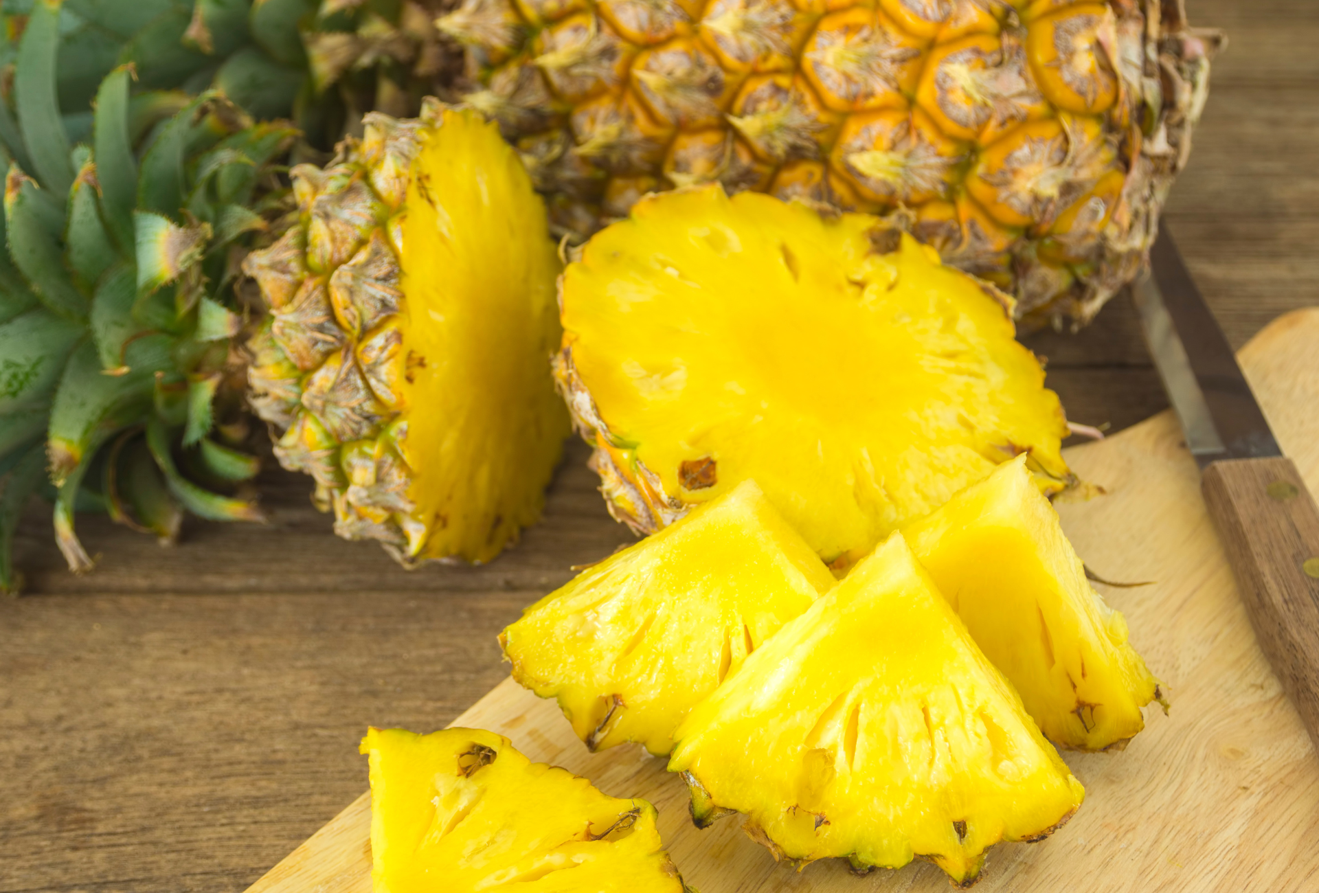 A pineapple is being sliced on a wooden cutting board.