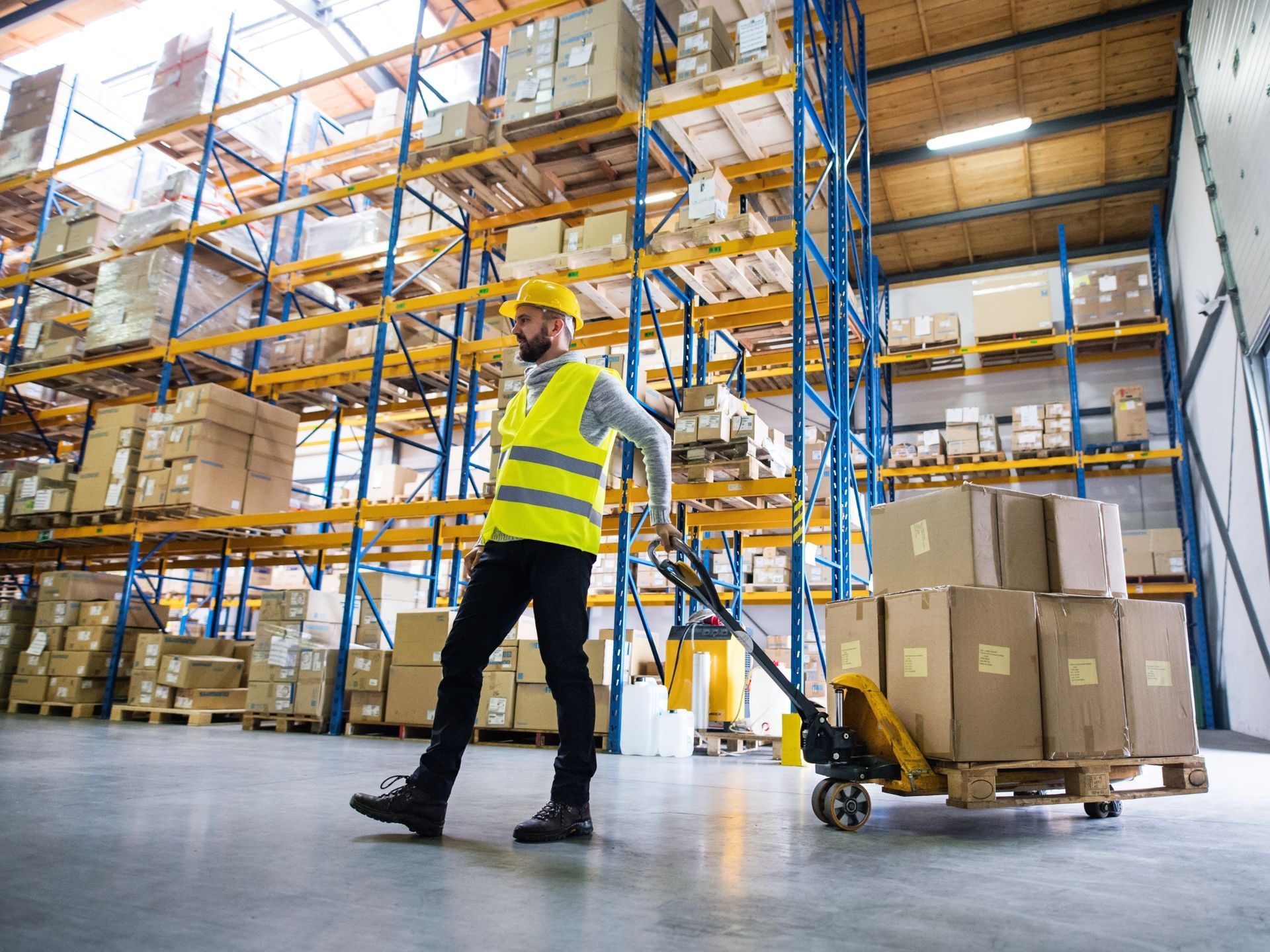 A man is pushing a pallet truck in a warehouse.