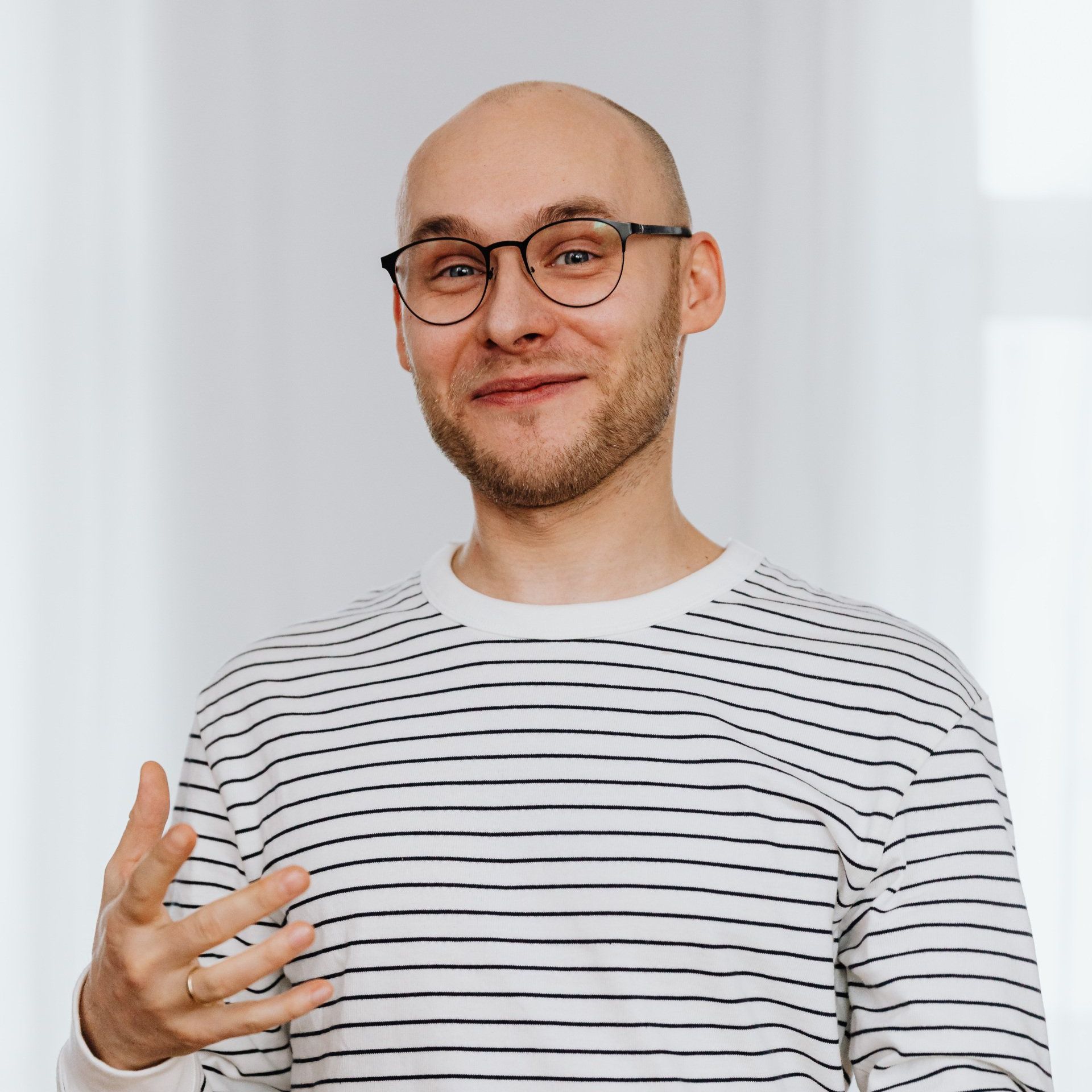A bald man wearing glasses and a striped shirt is smiling.