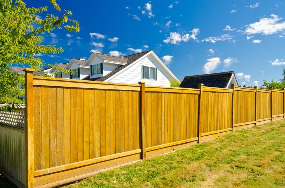 A Wooden Fence Surrounds a Lush Green Field in Front of a House — Perry's Timber & Fencing In Kiama, NSW