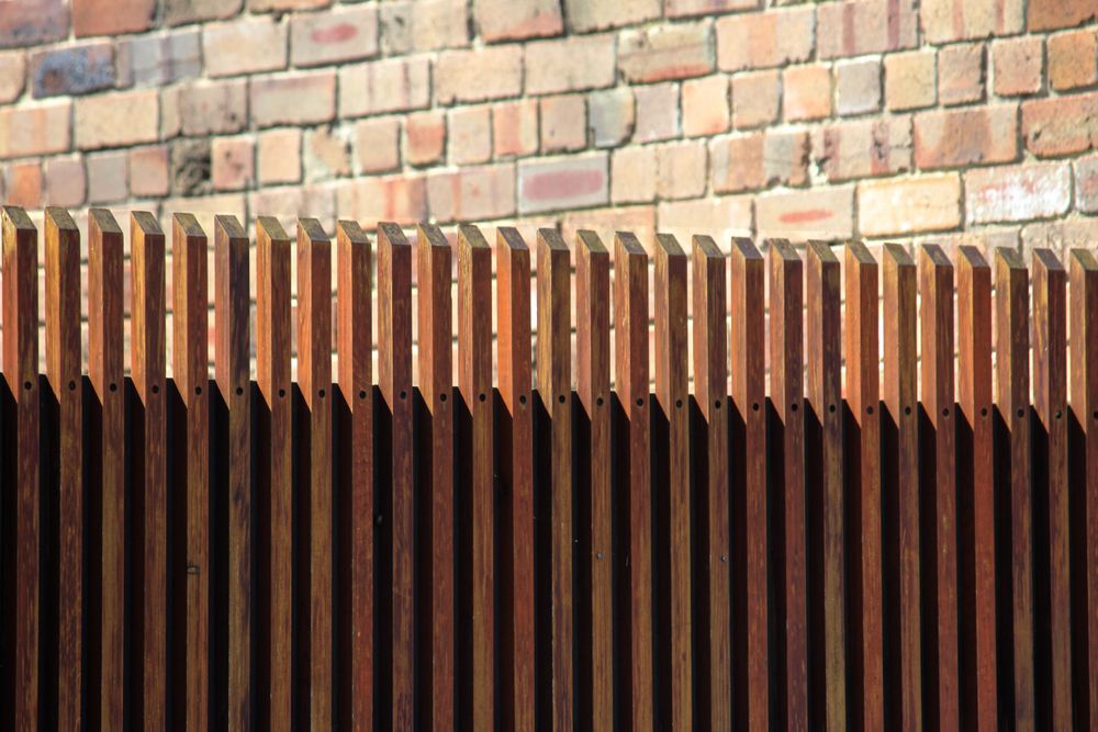 A Close Up of a Wooden Fence in Front of a Brick Wall — Perry's Timber & Fencing In Albion Park, NSW