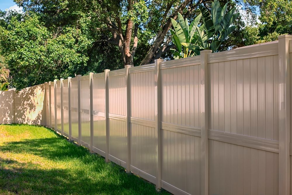 A Tan Vinyl Fence Surrounds a Lush Green Yard — Perry's Timber & Fencing In Thirroul, NSW