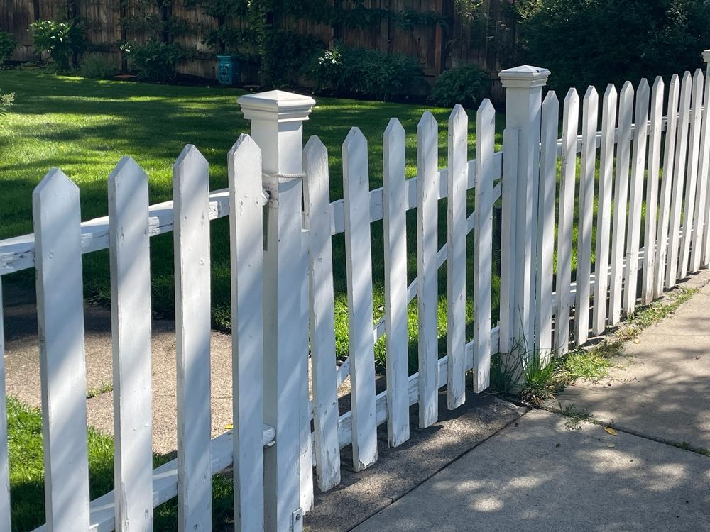 A White Picket Fence Along a Sidewalk in Front of a Lush Green Yard — Perry's Timber & Fencing In Thirroul, NSW