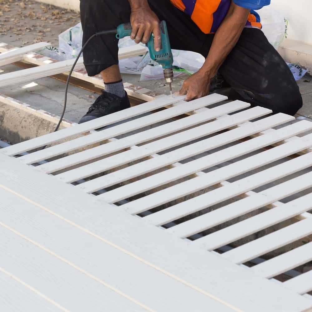 A Man is Using a Makita Drill on a White Fence — Perry's Timber & Fencing In Dapto, NSW
