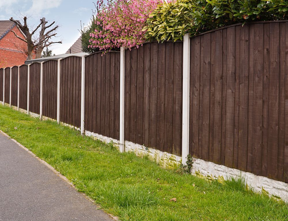 A Wooden Fence Surrounds a Lush Green Field Next to a Road — Perry's Timber & Fencing In Dapto, NSW