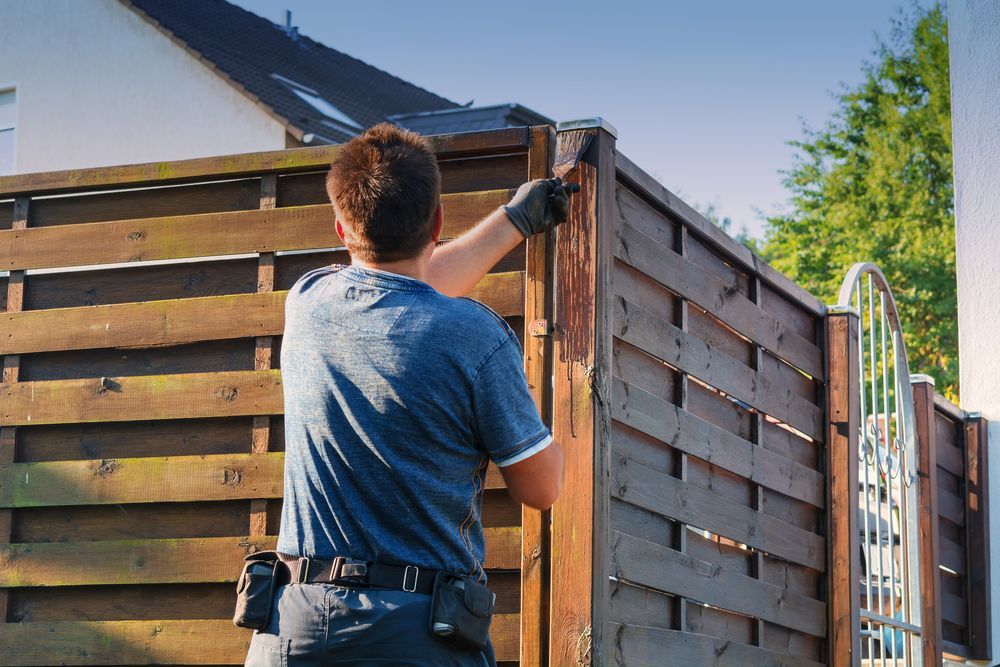 A Man is Standing Next to a Wooden Fence — Perry's Timber & Fencing In Thirroul, NSW