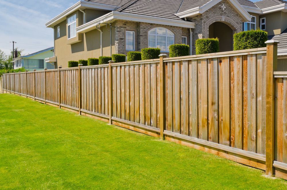 A Wooden Fence Surrounds A Lush Green Lawn In Front Of A House — Perry's Timber & Fencing In Dapto, NSW