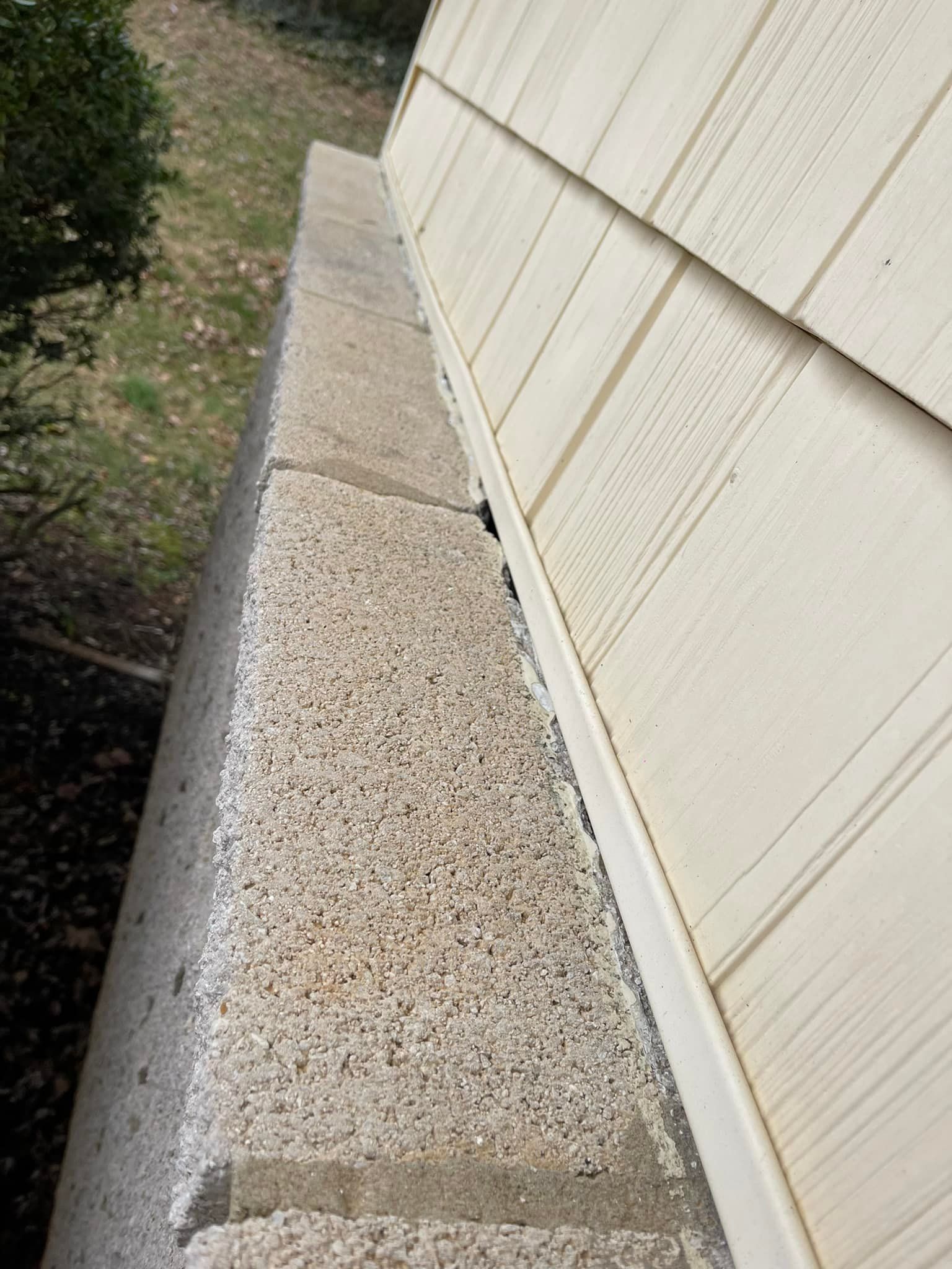 Concrete ledge next to a light-colored siding wall, outdoors in a grassy setting.