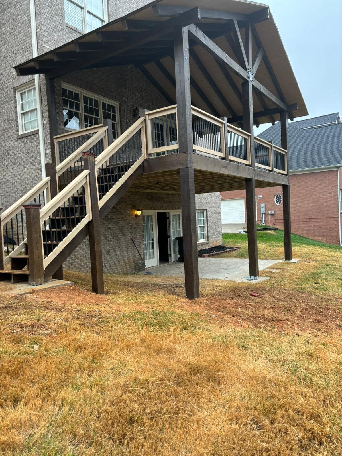 Brown wooden deck with a roof, steps, and railing on a brick house.