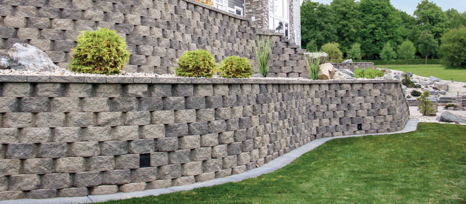 Stone retaining wall with greenery and lawn.