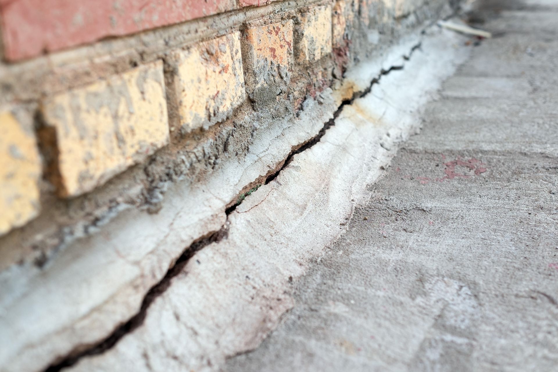 Cracked concrete and white mortar along a brick wall base, showing damage at the foundation edge