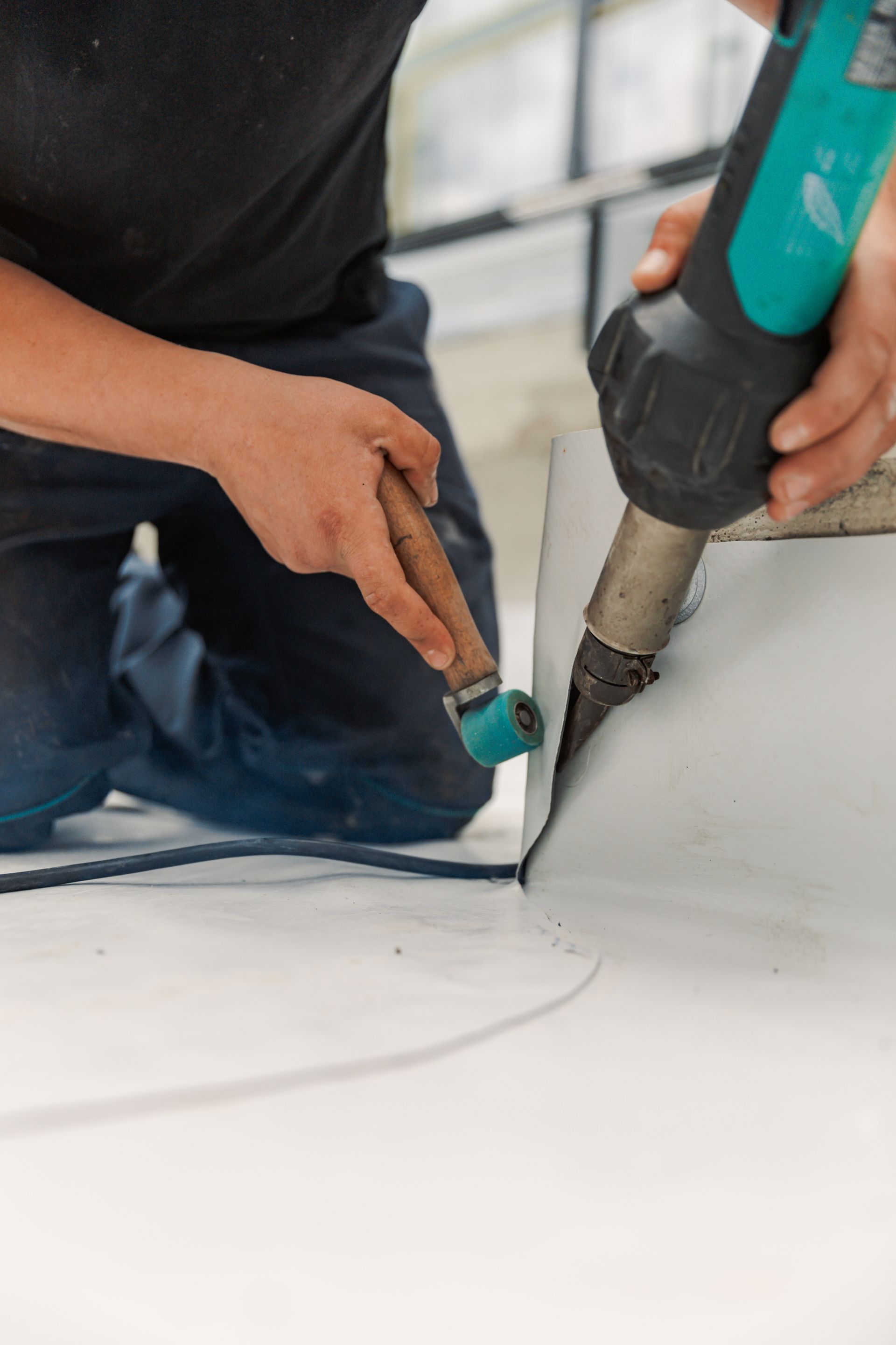 Person using a heat gun to weld a seam on a white roofing membrane.