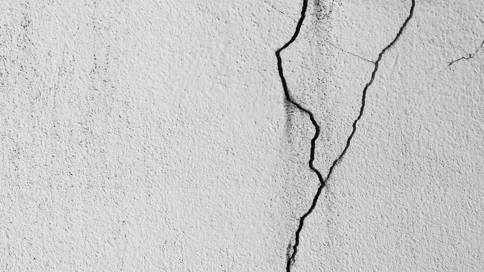 Close-up of a cracked white wall with a jagged vertical fissure
