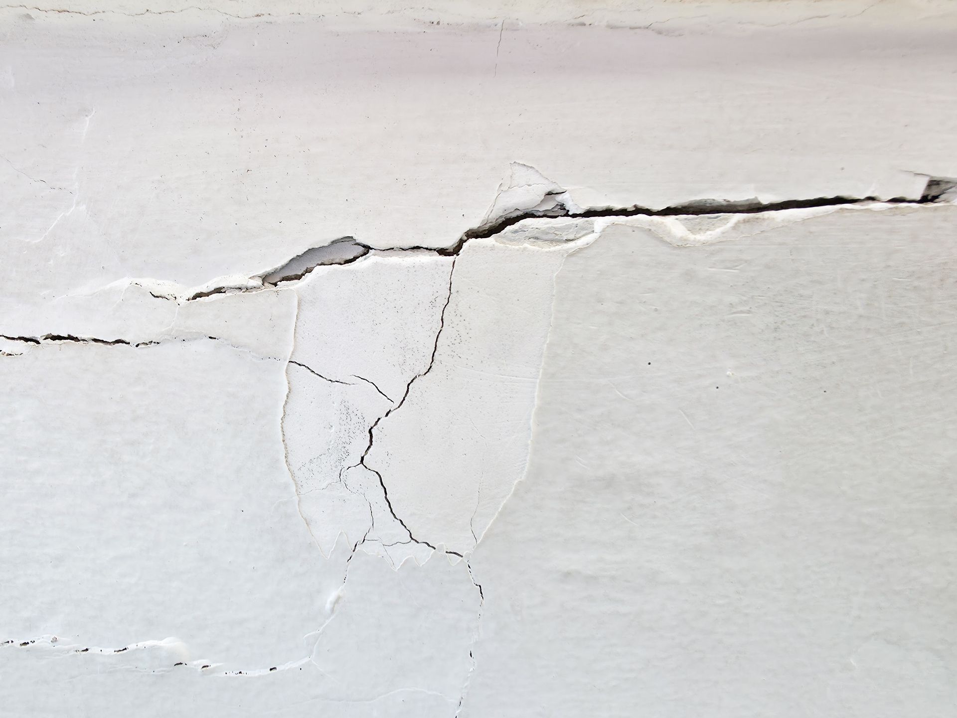 Cracked white wall with peeling paint and a long horizontal fracture