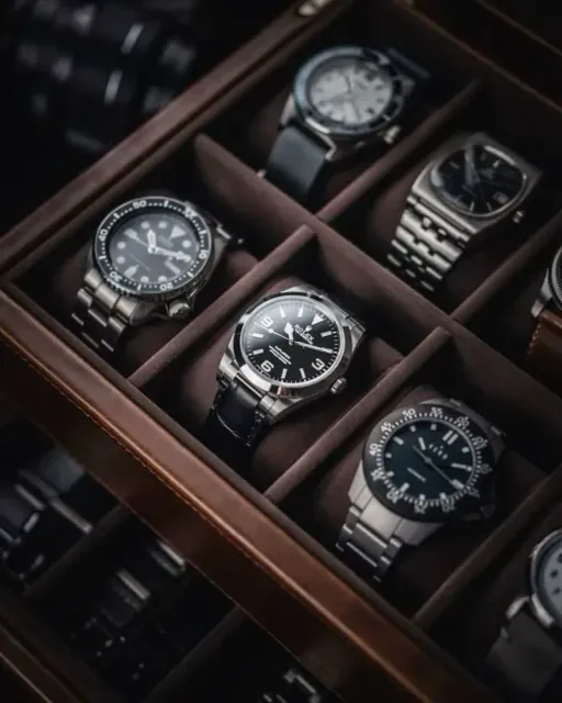 Watch collection in a wooden display case with various metal and leather band styles.