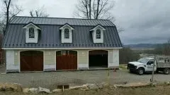 White barn-style house with three dormers and a parked white SUV on a cloudy day