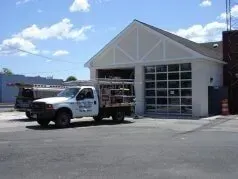 White utility truck parked outside a garage with large glass doors on a sunny day