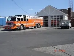 Orange and white fire truck parked outside a fire station on a sunny day
