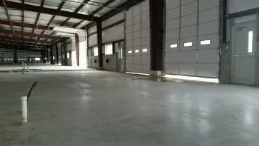 Empty industrial warehouse interior with concrete floor, metal beams, and large closed garage doors