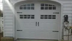 White garage door with arched top and small windows, set in gray siding