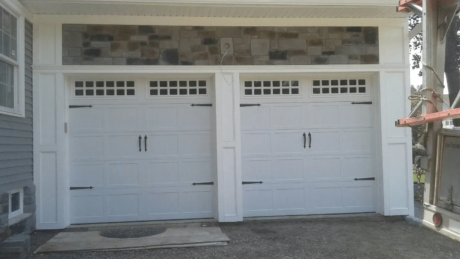 Two white garage doors on a house exterior with small windows above each door