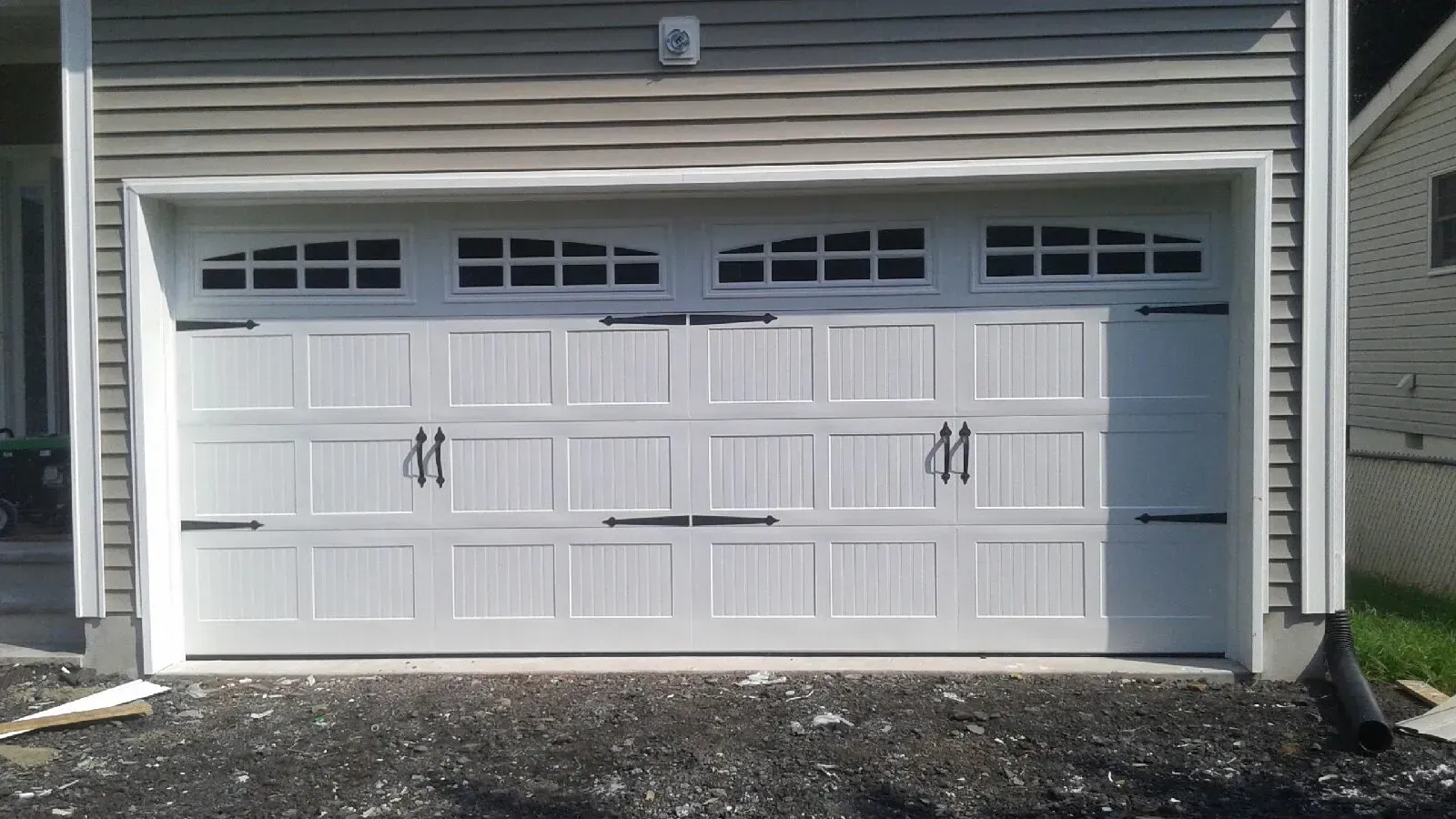 White double garage door on a gray house exterior with small windows and brick paving in front