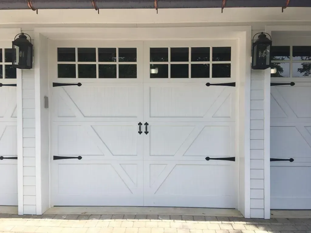 White garage door with black hardware and small windows on a house exterior