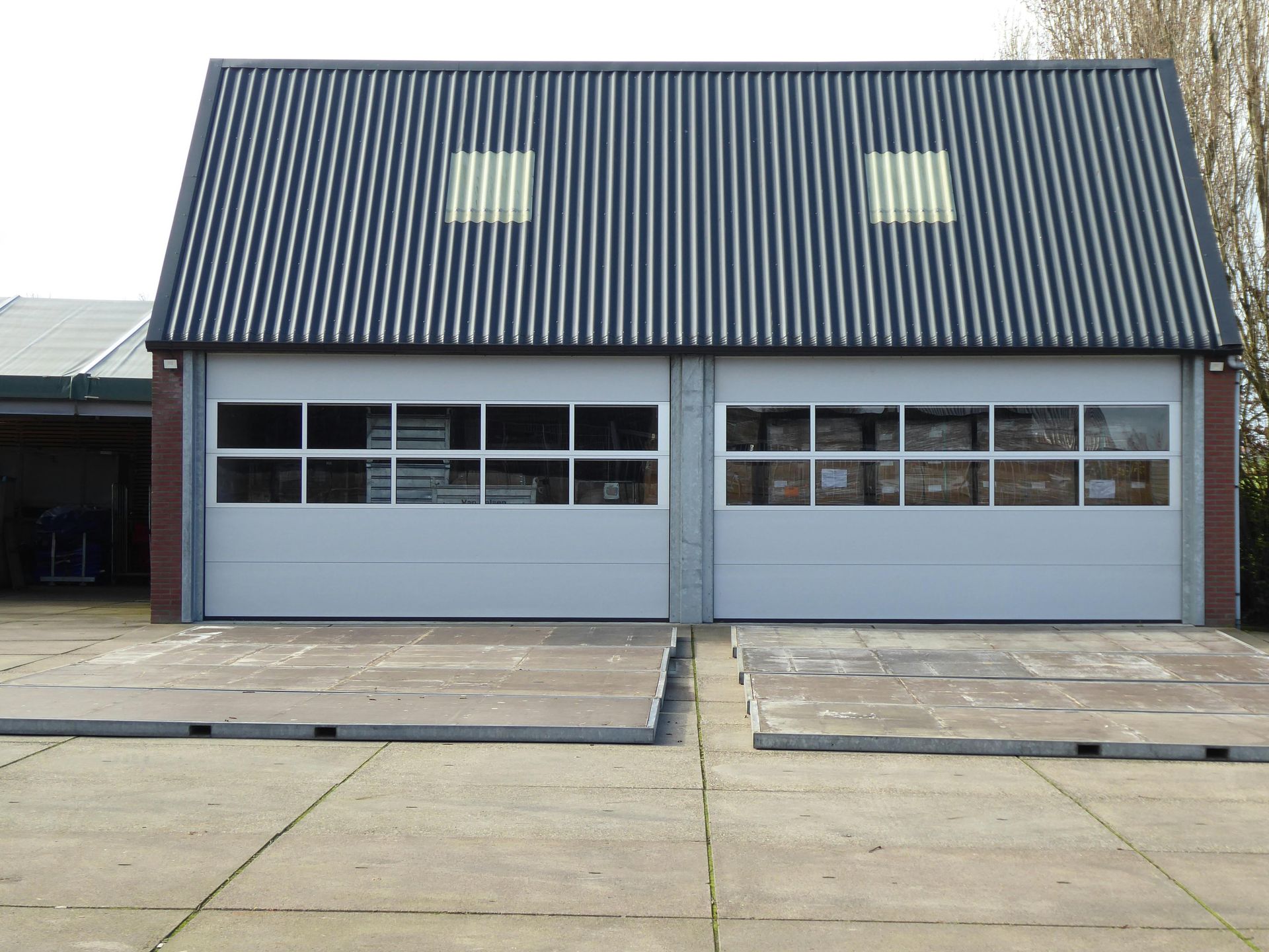 Gray building with a steep dark roof and two garage-style doors facing a concrete lot.