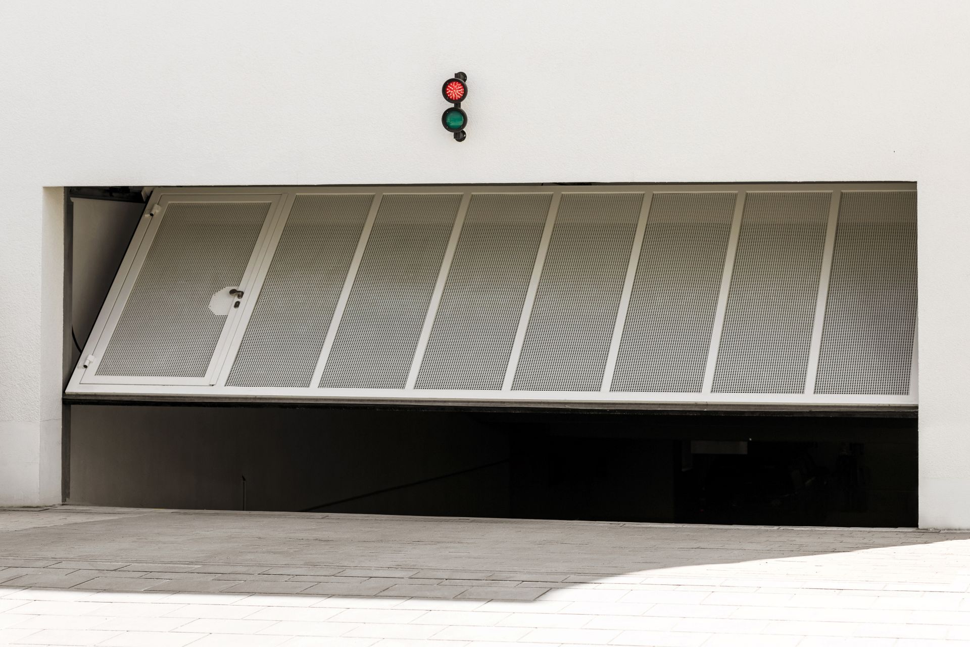 Tilted white metal garage door with a red-and-green traffic light above it
