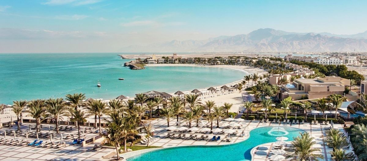 An aerial view of a beach resort with a large swimming pool surrounded by palm trees.